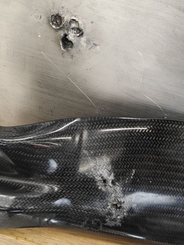 Three impact craters in an aluminium block above a carbon-fibre UAV propeller with impact damage